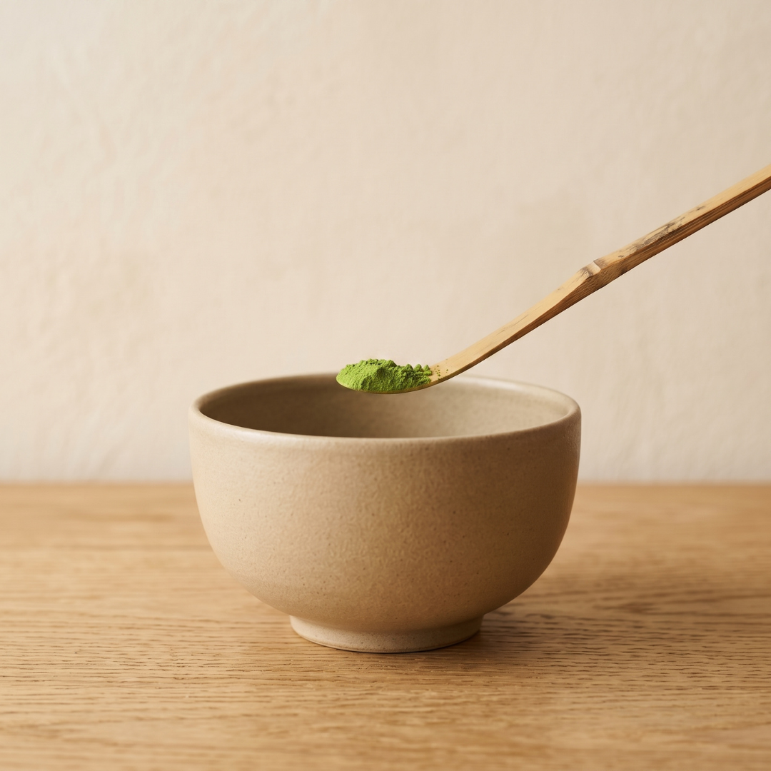 Biologische ceremonial matcha poeder op een traditionele bamboe theelepel (chashaku) boven een kom matcha.