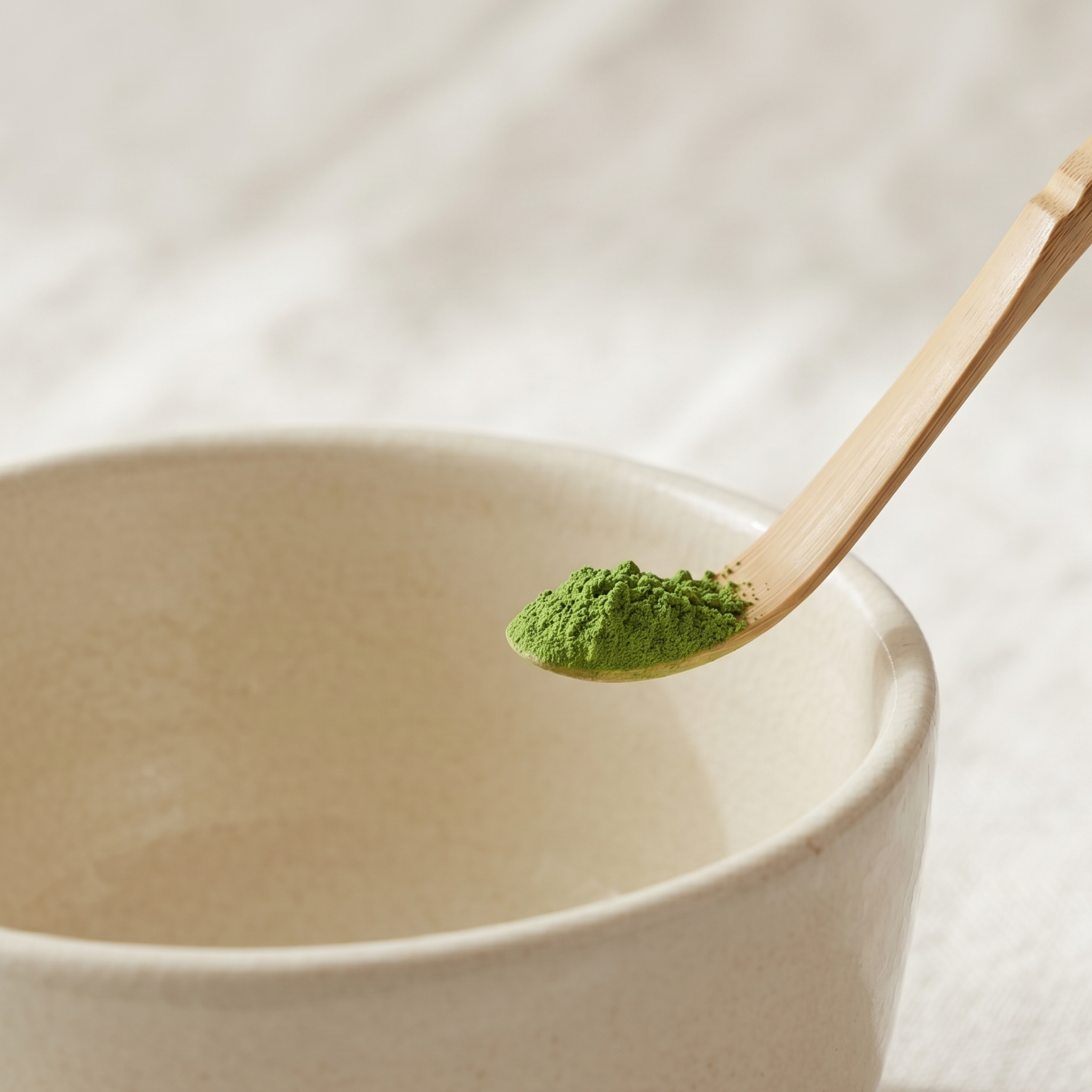Biologische ceremonial matcha poeder op een traditionele bamboe theelepel (chashaku) boven een kom matcha.