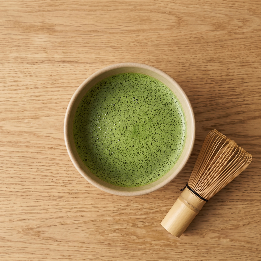 Opgeklopte biologische ceremonial matcha in een kom met ernaast een bamboe whisk.